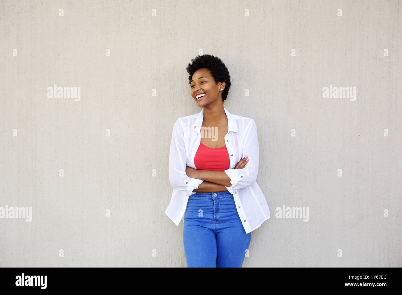 Portrait of a smiling young african woman with arms crossed standing ...