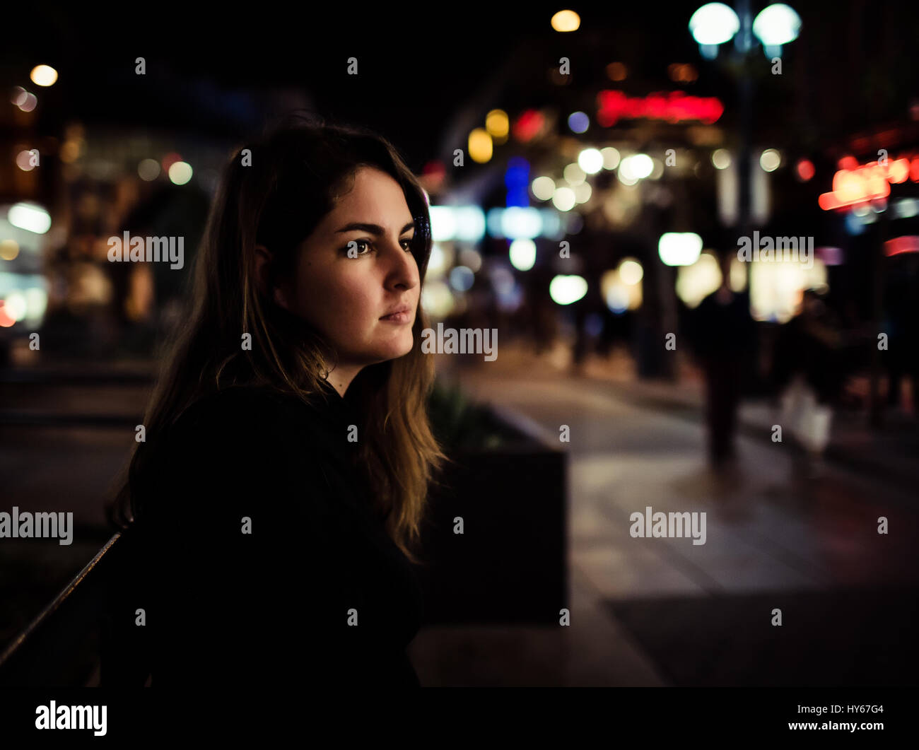 A girl sitting on a bench in the busy 3rd street promenade in Santa Monica, maybe waiting for someone or just having alone time. Stock Photo