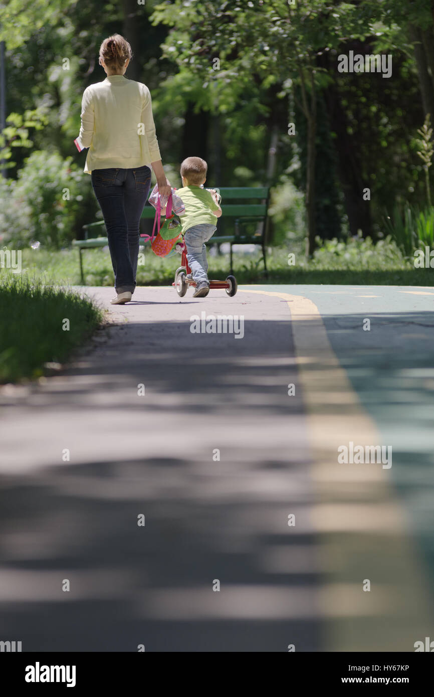 Kid with a push scooter rolling on the line next to his mother Stock Photo