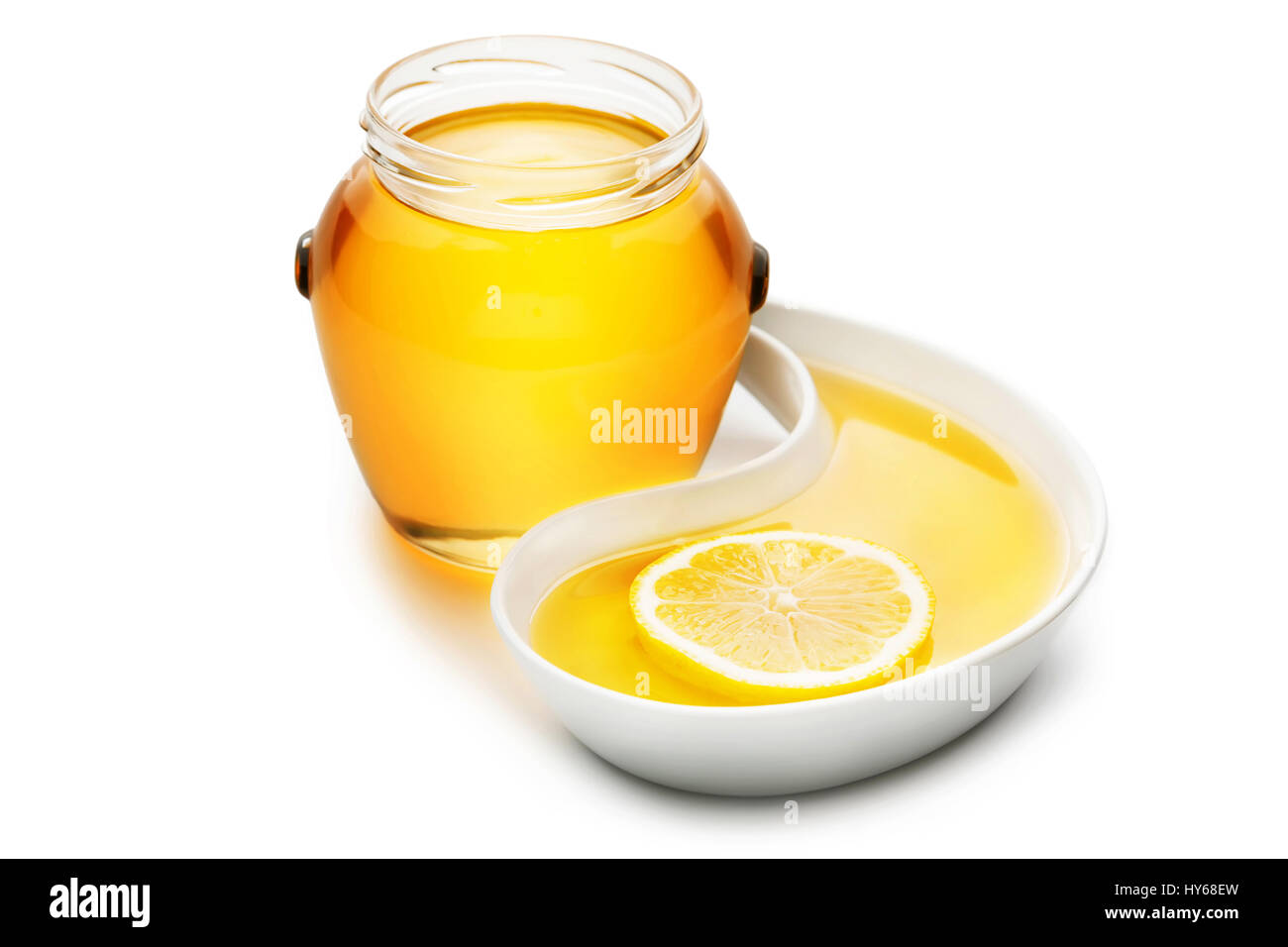 Jar of honey next to a slice of lemon in a tear shaped tray, isolated ...