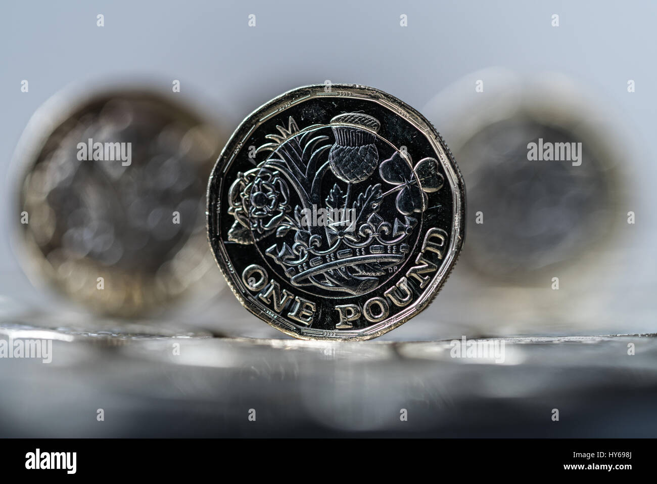 new pound coin introduced in Britain in 2017, front, standing on a layer of coins within two other coins in the distance (trio) Stock Photo