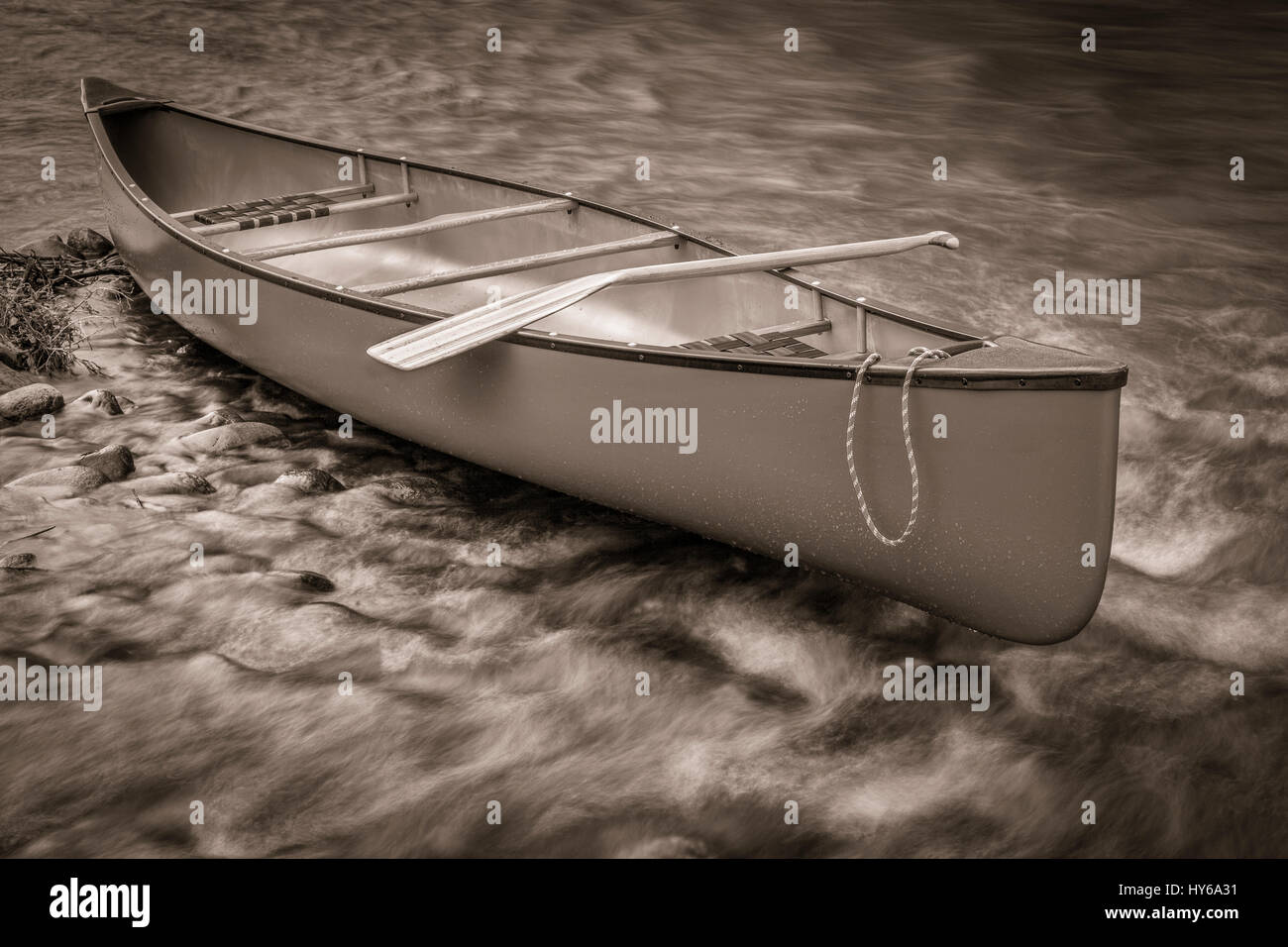 canoe with a paddle on s shore of shallow and rocky river, retro sepia toning Stock Photo