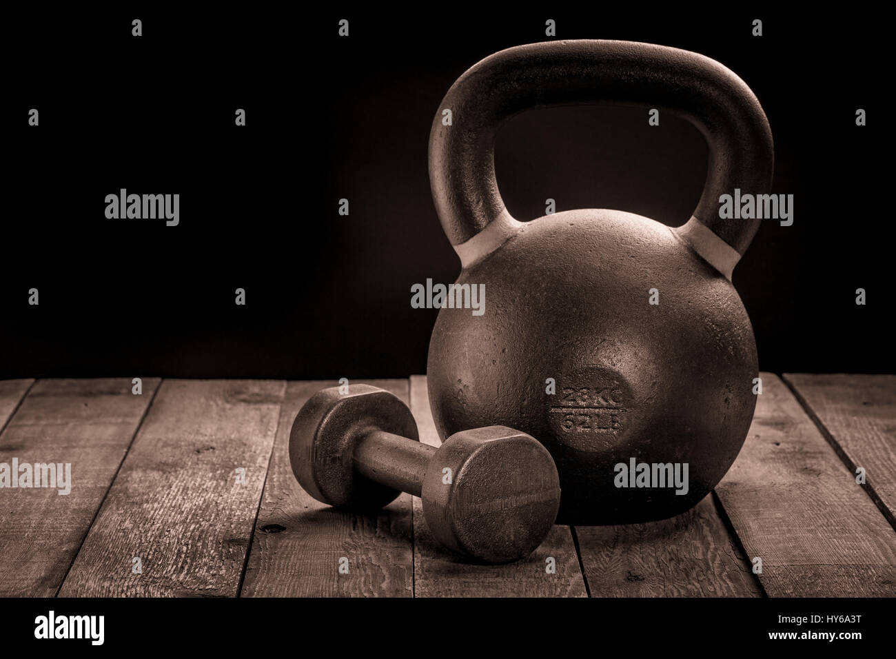 exercise weights - a heavy iron kettlebell and dumbbell on a wooden rustic deck - a home gym concept, sepia toning Stock Photo