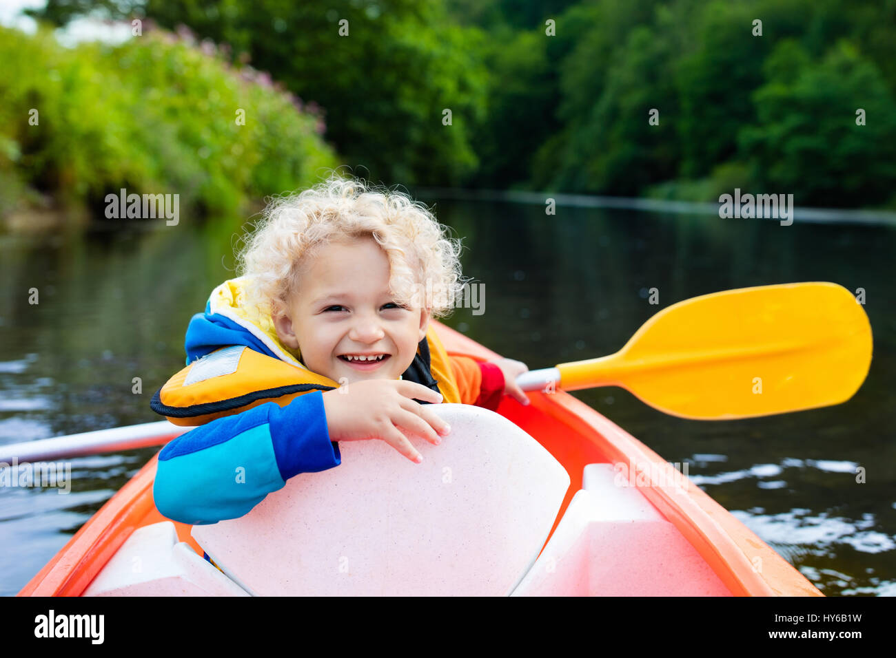 Happy kid enjoying kayak ride on beautiful river. Little curly toddler ...