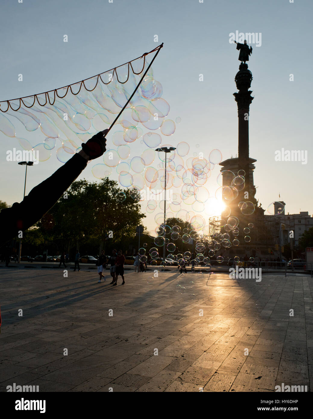 street artist blowing soap bubbles towards setting sun at  Plaça Portal de la Pau, Mirador de Colón, Barcelona, Katalonien, Spanien Stock Photo