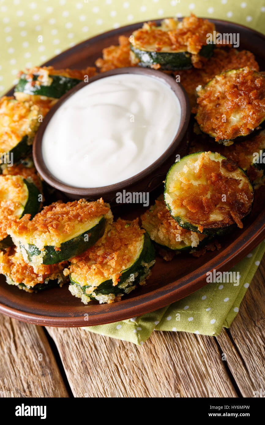 Homemade zucchini slices in breadcrumbs with sour cream close-up on the table. Vertical Stock Photo