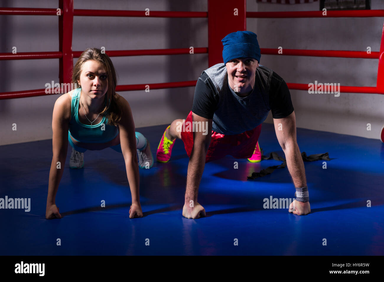 Young sporty boxing couple in sportswear doing pushup in regular boxing ring in a gym Stock
