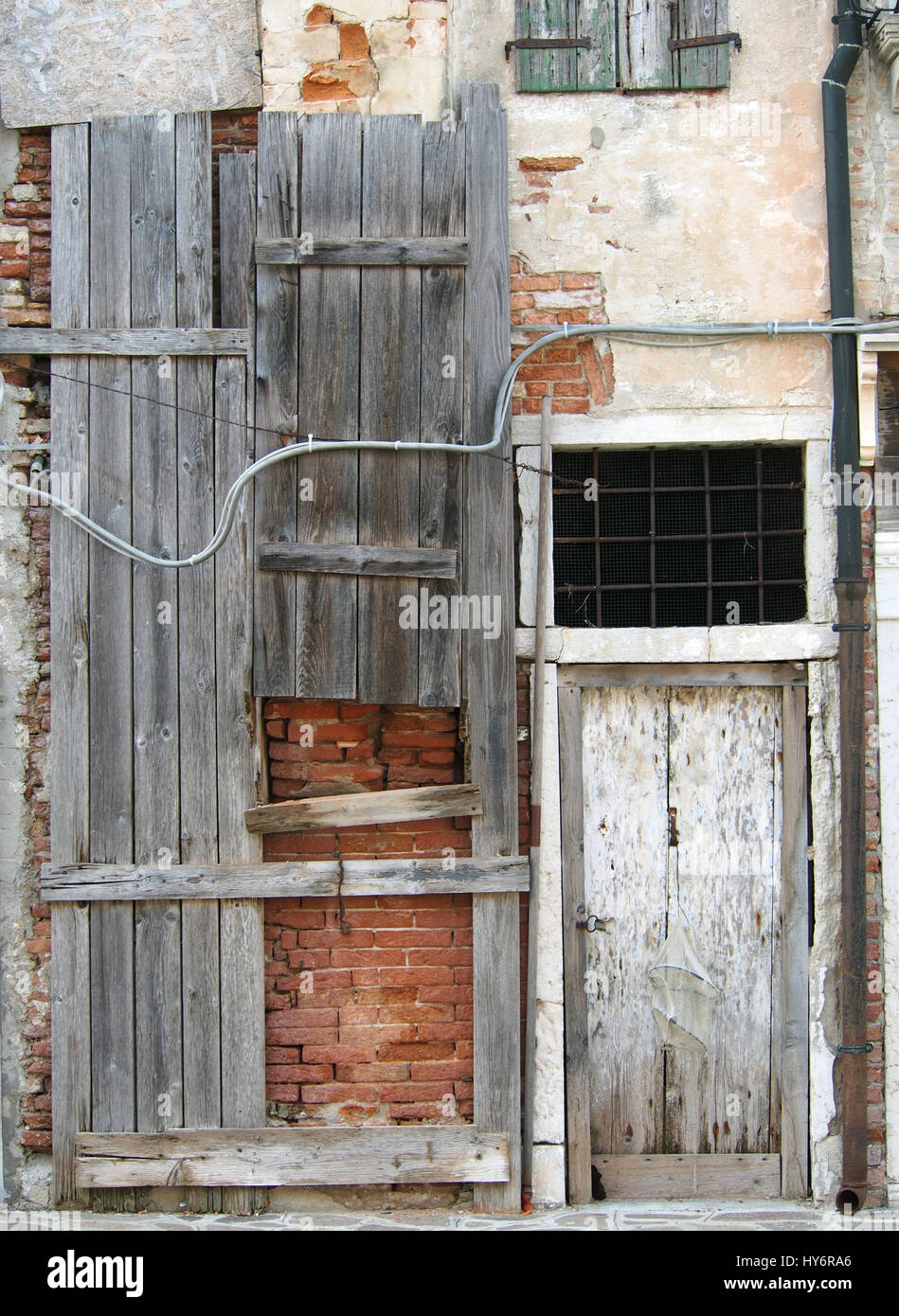 Old boarded up house with weatherd grey planks, brick walls and a white door Stock Photo