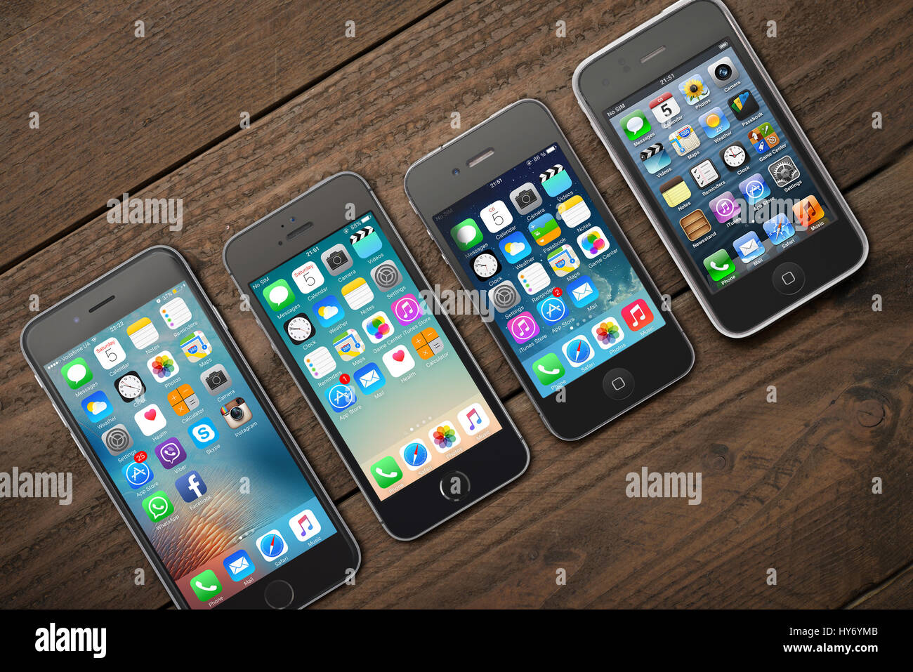 Kiev, Ukraine - March 05, 2016: Front view of a space grey color iPhones 6, 5s, 4 and 3gs generation showing the home screens on wooden background. Stock Photo