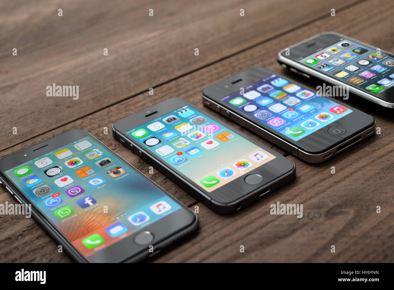 Kiev, Ukraine - March 05, 2016: Front view of a space grey color iPhones 6, 5s, 4 and 3gs generation showing the home screens on wooden background. Stock Photo
