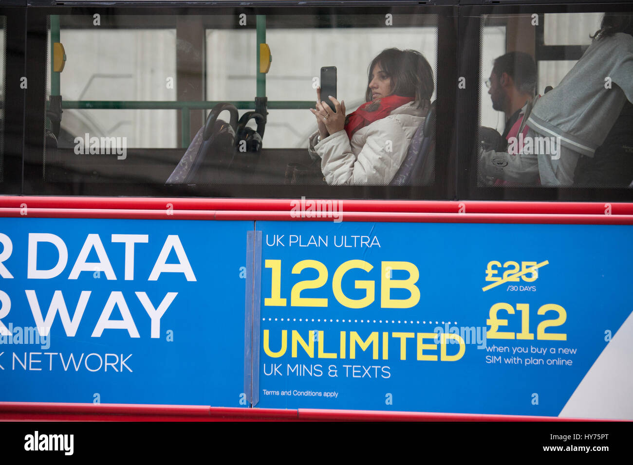 Female looking at mobile phone on top deck of bus, with advert for mobile phone data on side of bus Stock Photo