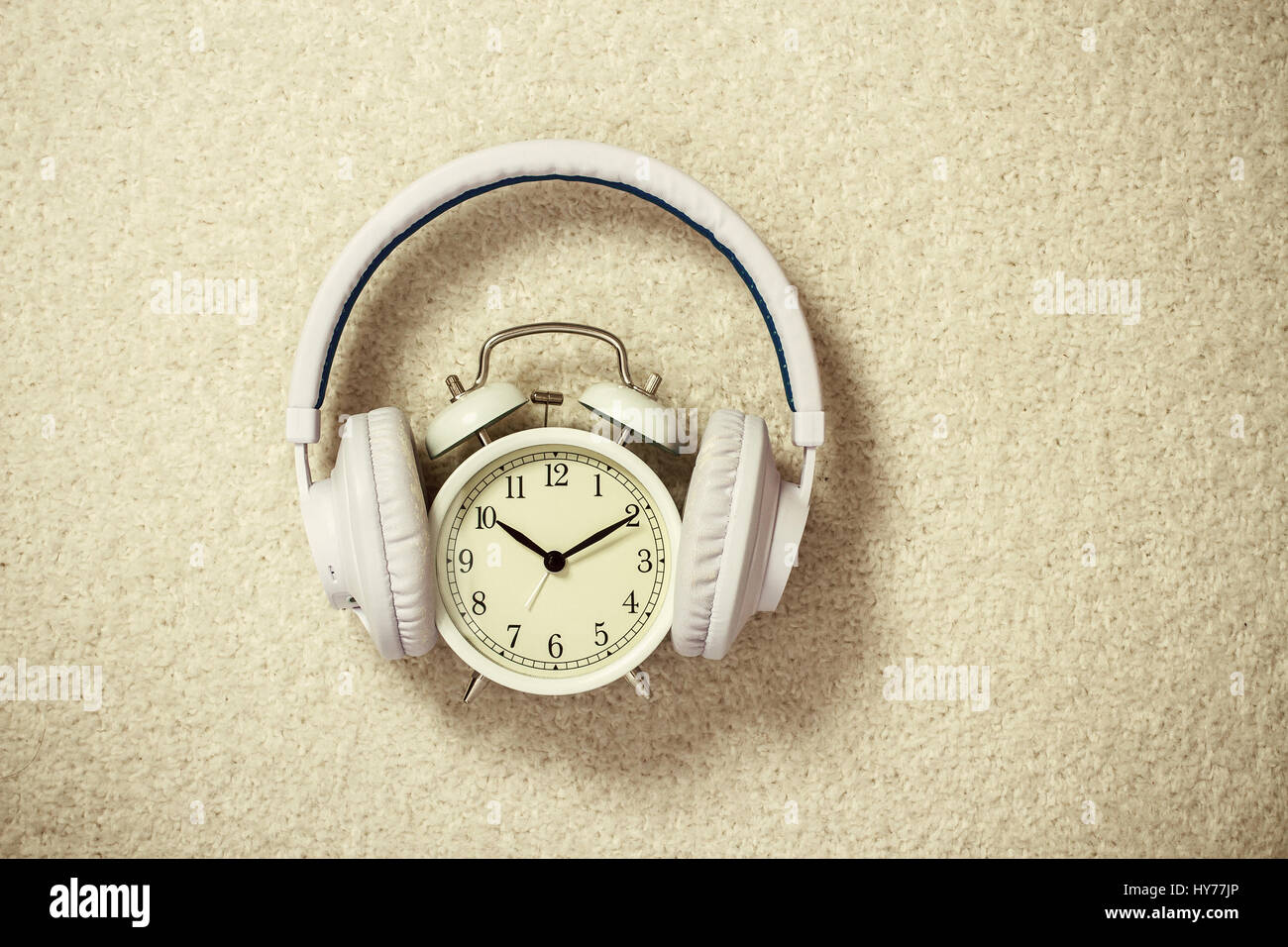 Retro alarm clock with white headphones on beige background Stock Photo