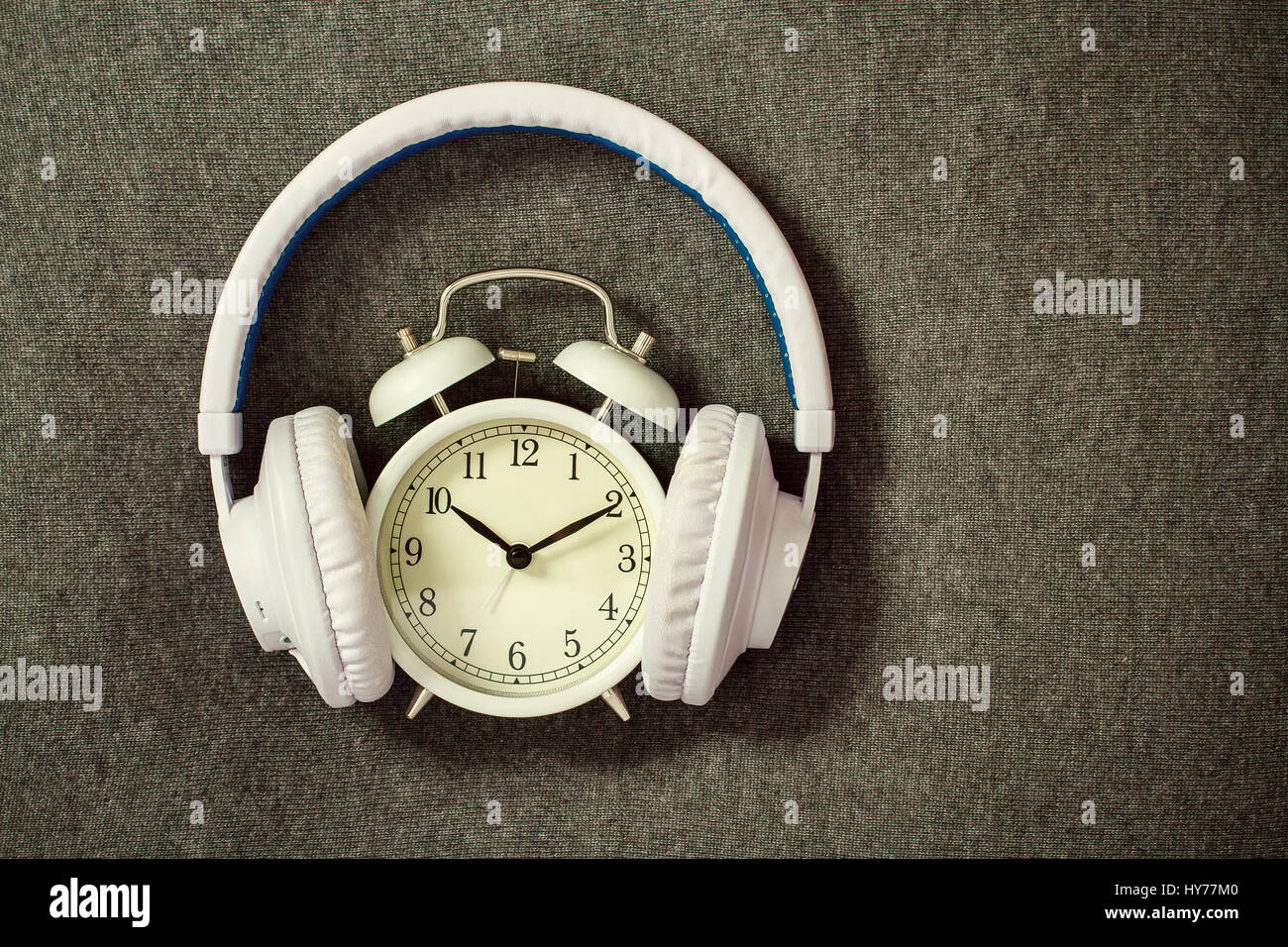 Retro alarm clock with white headphones on gray knitting Stock Photo
