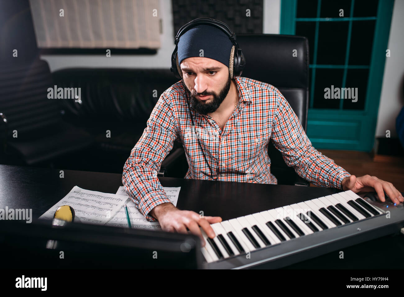 Sound producer in headphones work with musical keyboard in studio