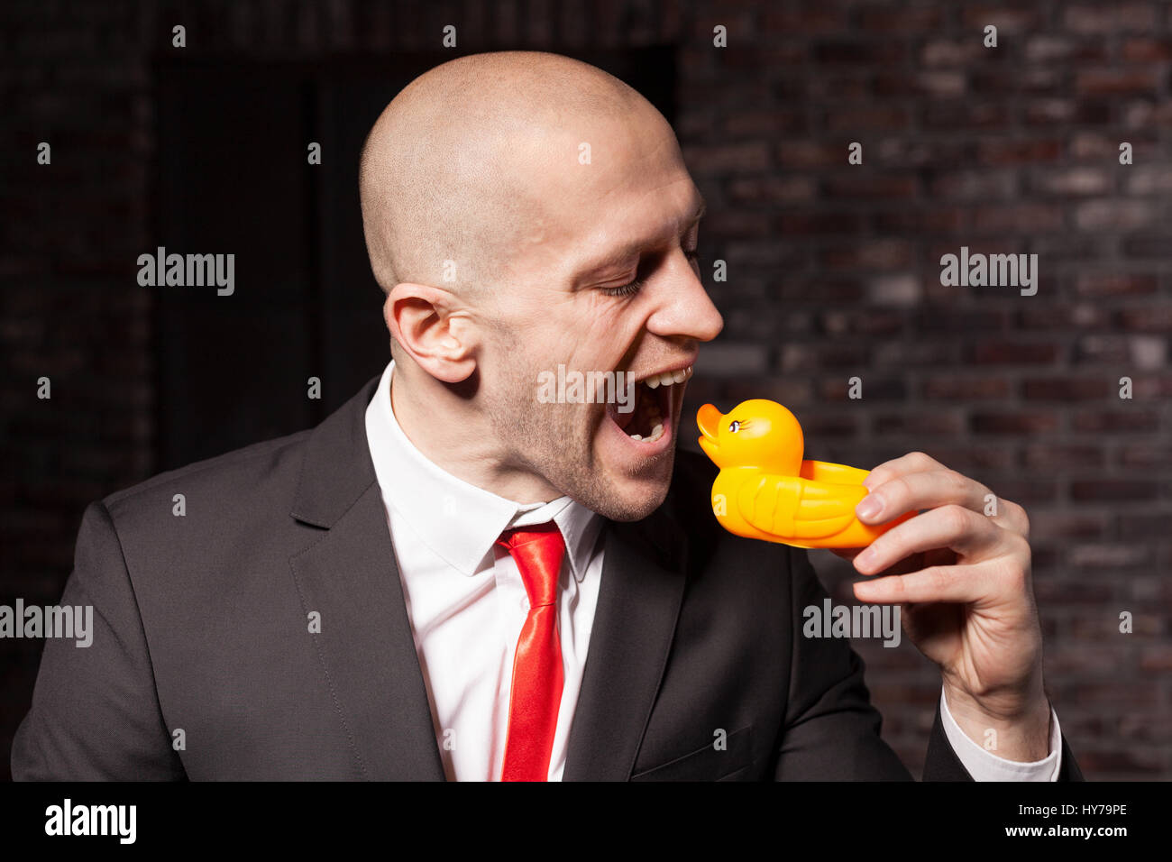 Contract killer in suit and red tie is going tp eat a little toy duck Stock Photo