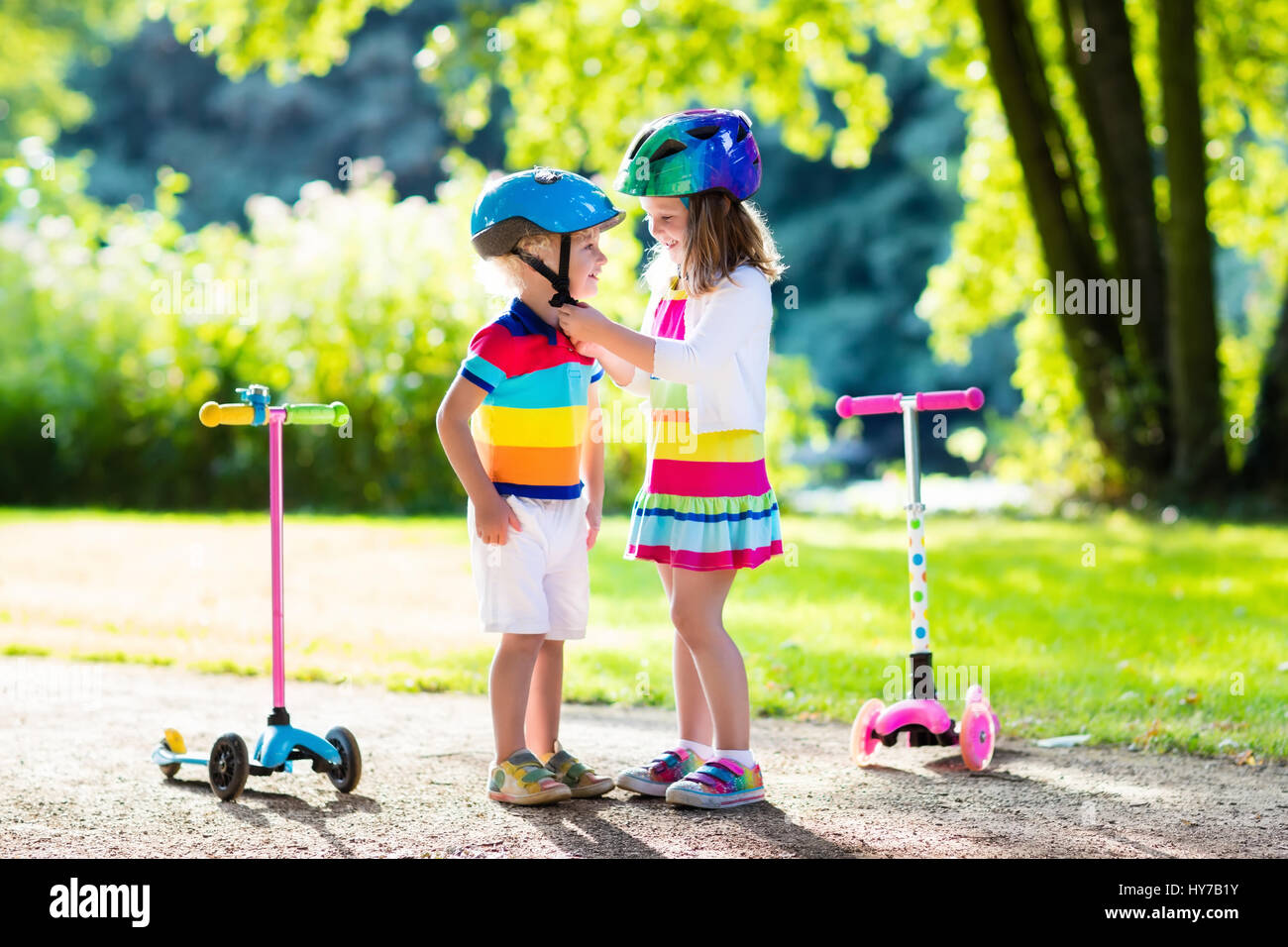 Children learn to ride scooter in a park on summer day. Preschooler