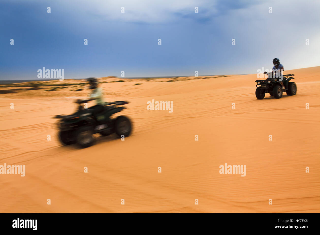 A couple of fast quadbikes riding through the remote sand dunes at speed blurred with panning making drivers unrecognizable. Stock Photo