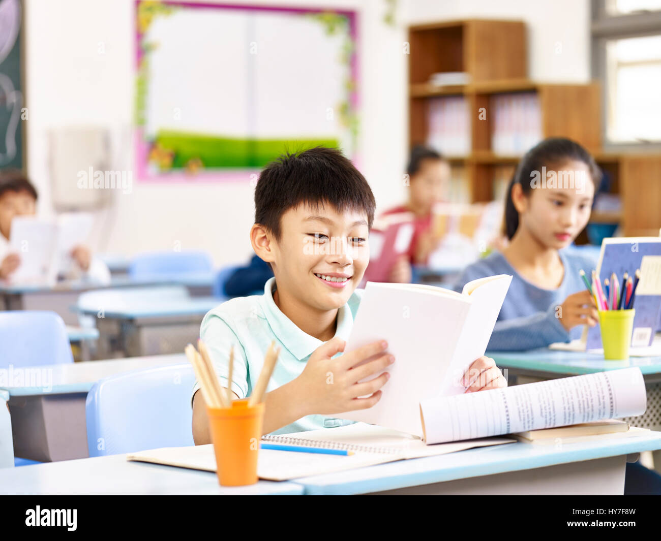 asian elementary school students reading book in classroom, happy and smiling. Stock Photo