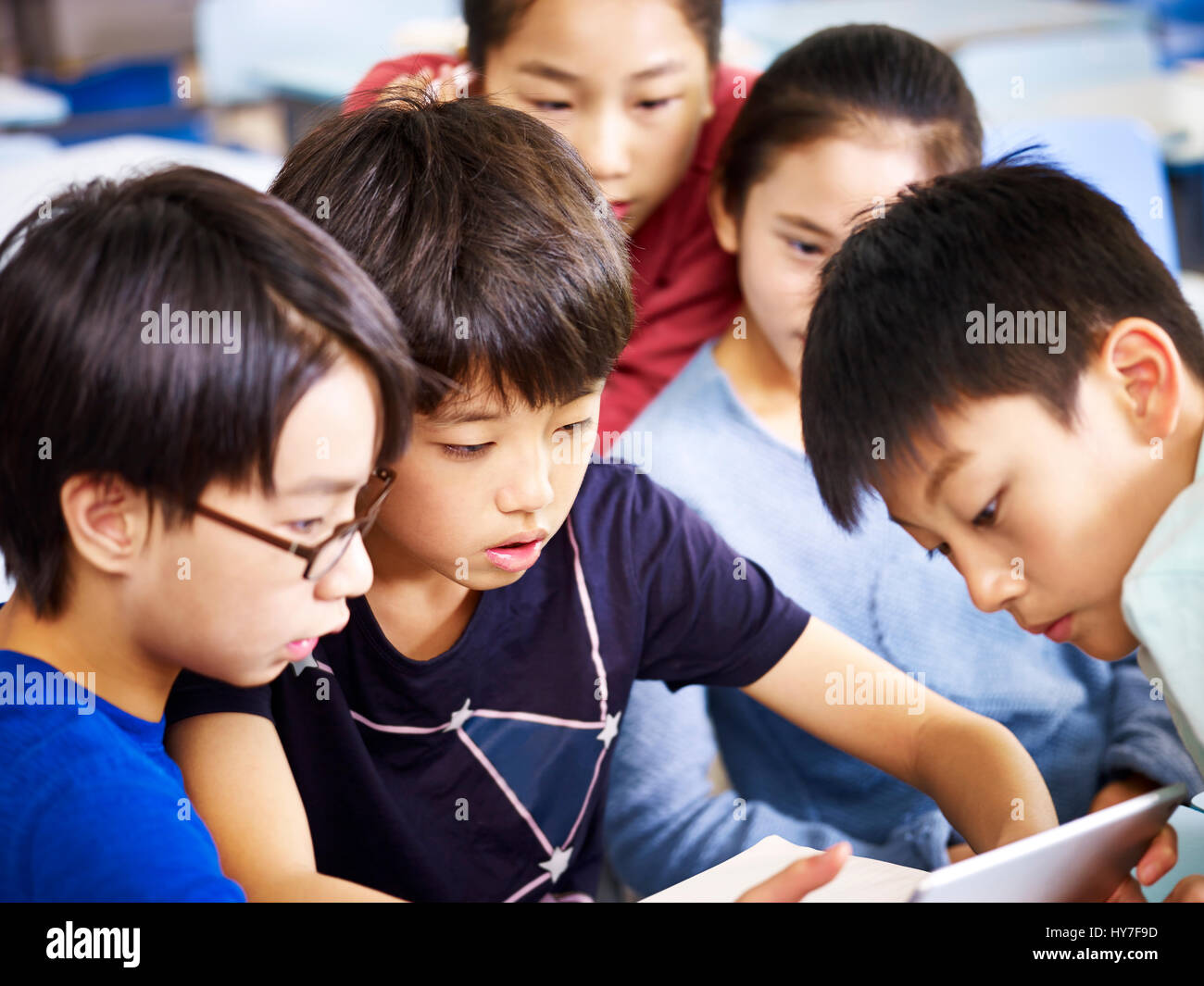 group of asian elementary schoolchildren playing game using tablet together. Stock Photo