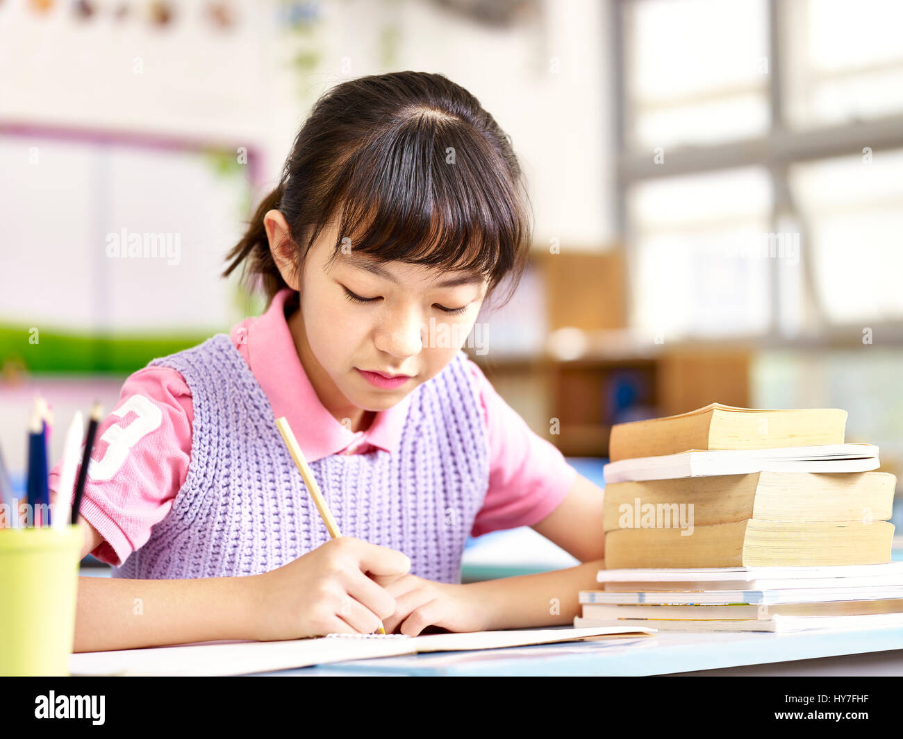 asian elementary schoolgirl studying or doing course work in classroom. Stock Photo