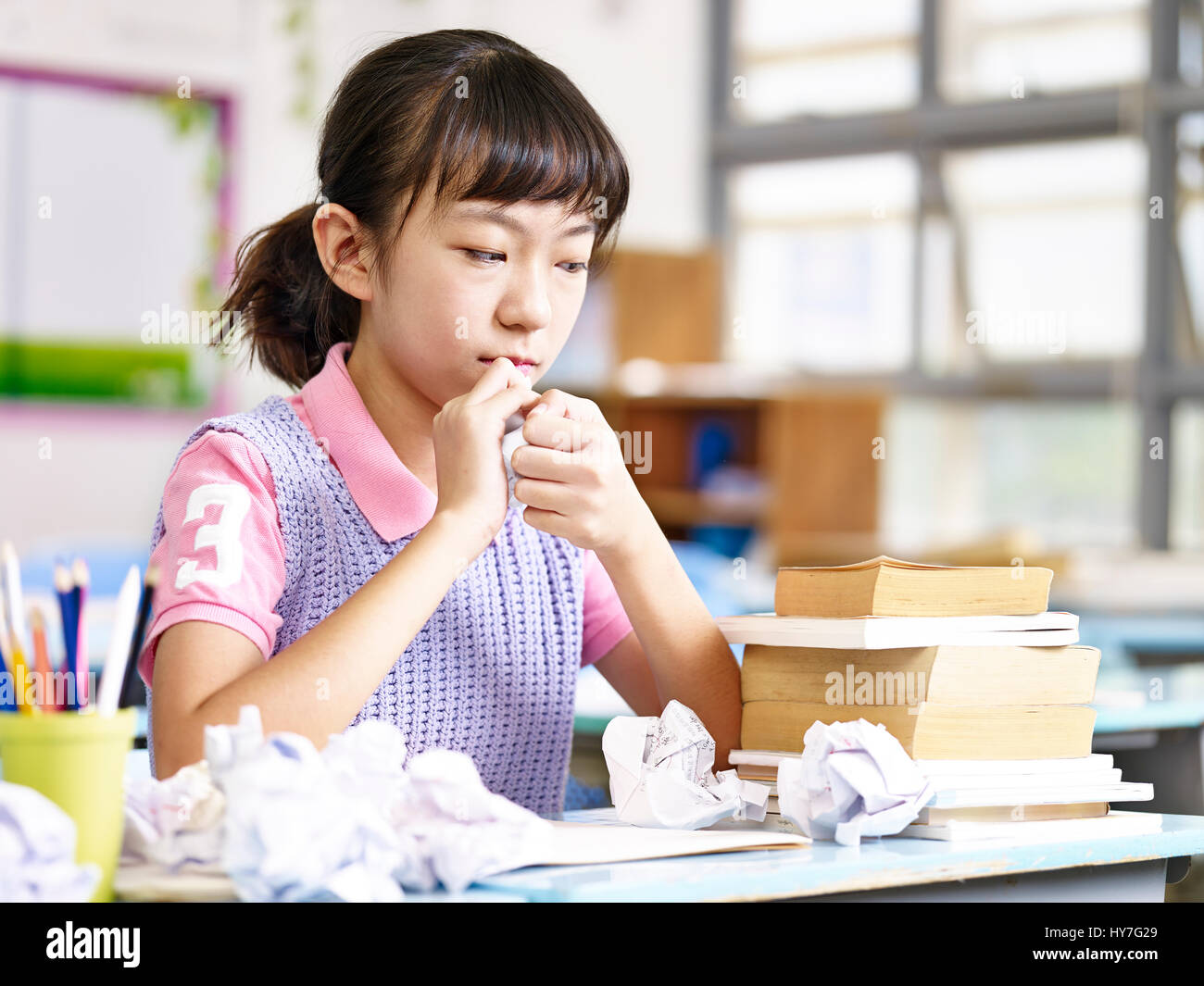 asian primary school schoolgirl crumbling a piece of paper out of frustration. Stock Photo