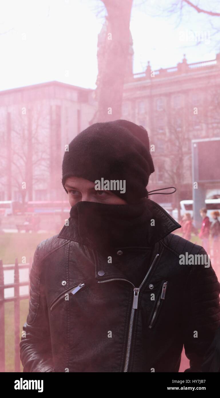 Belfast, Northern Ireland, UK. 1st April, 2017. A protester covers his face as a smoke bomb is set off during an anti fascist protest in Belfast Credit: Conall Kearney/Alamy Live News Stock Photo