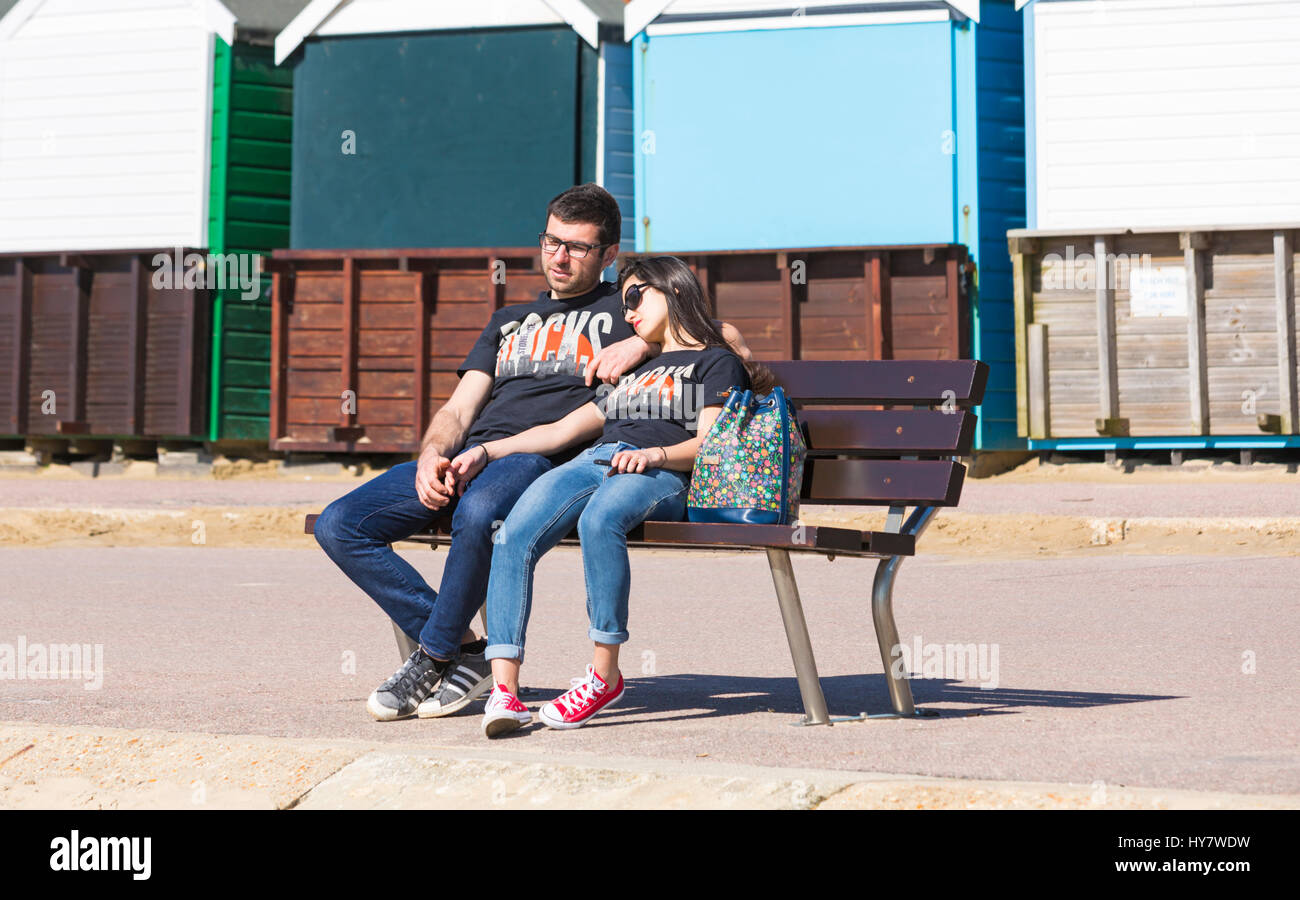 Bournemouth, Dorset, UK. 2nd April 2017. UK weather: lovely warm sunny day as visitors head to the seaside to make the most of the sunshine at Bournemouth beaches. Couple sitting on bench  relaxing and enjoying the sun on Bournemouth promenade wearing matching Stonehenge Rocks t-shirts and jeans. Credit: Carolyn Jenkins/Alamy Live News Stock Photo