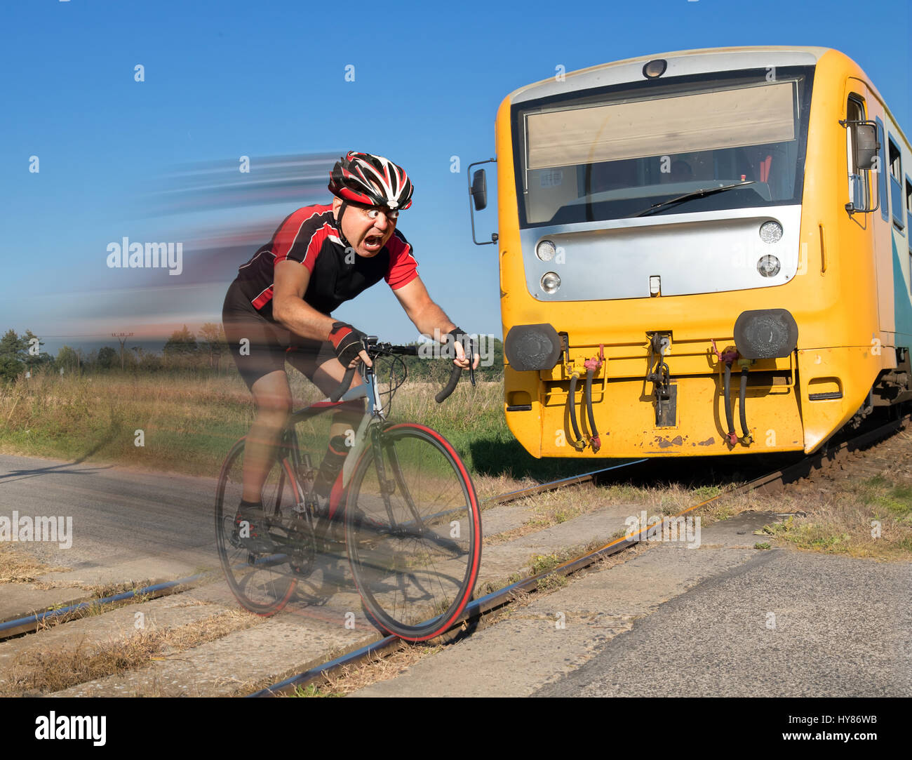 Terrified cyclist is rushing before by train on the tracks. Shocked biker ride a railway crossing in front of an approaching train. Stock Photo