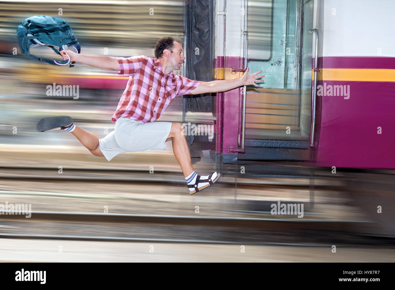 Tourist with bag running behind the train. A man runs for a moving wagon. Backpacker hurries for train departing from the station. Stock Photo