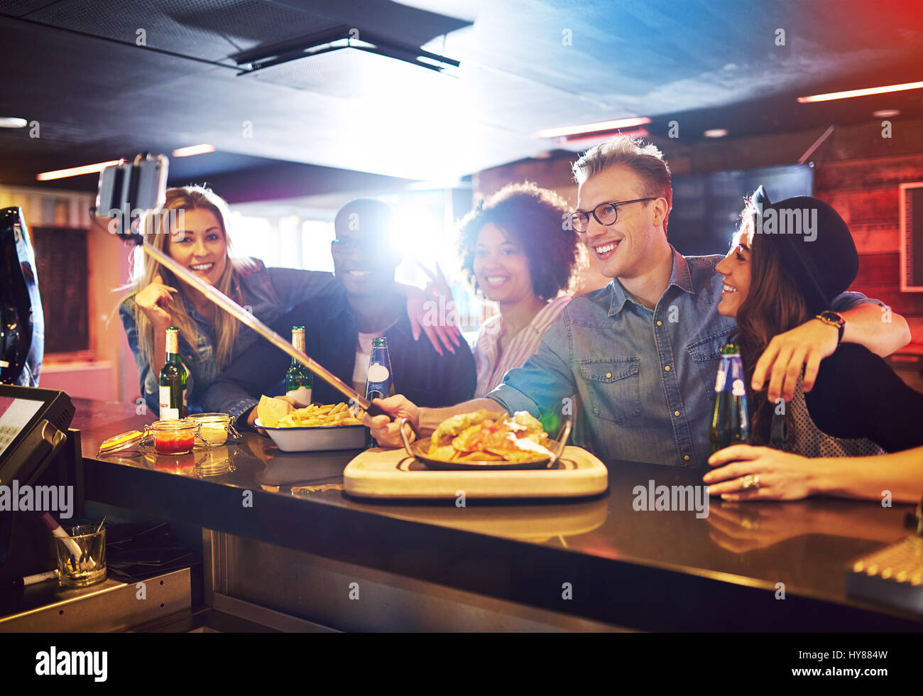 Happy group of friends posing for a selfie in the bar while having a drink and food. Horizontal indoors shot. Stock Photo