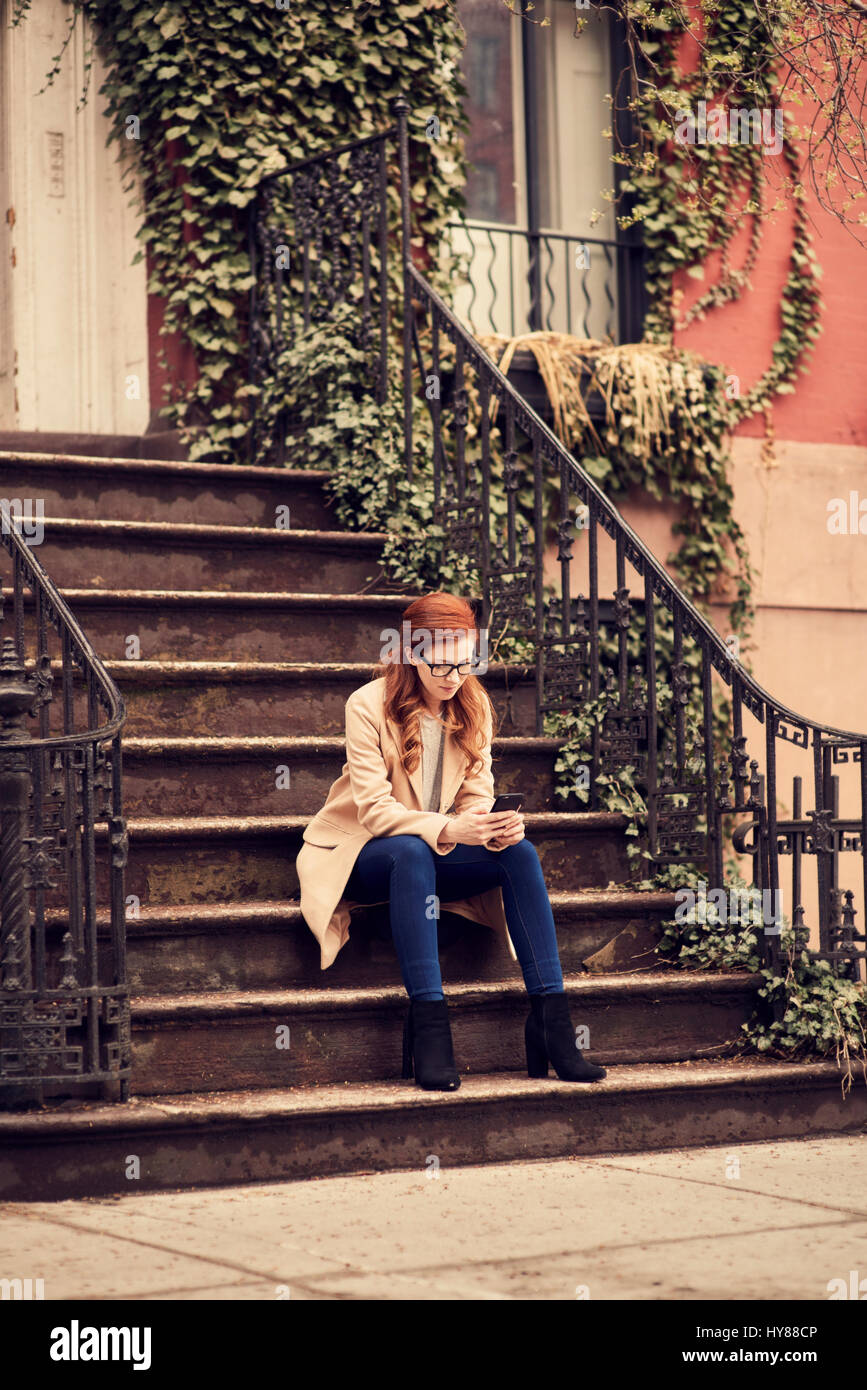 Young fashionable women sitting on steps on her smartphone in New York city Stock Photo