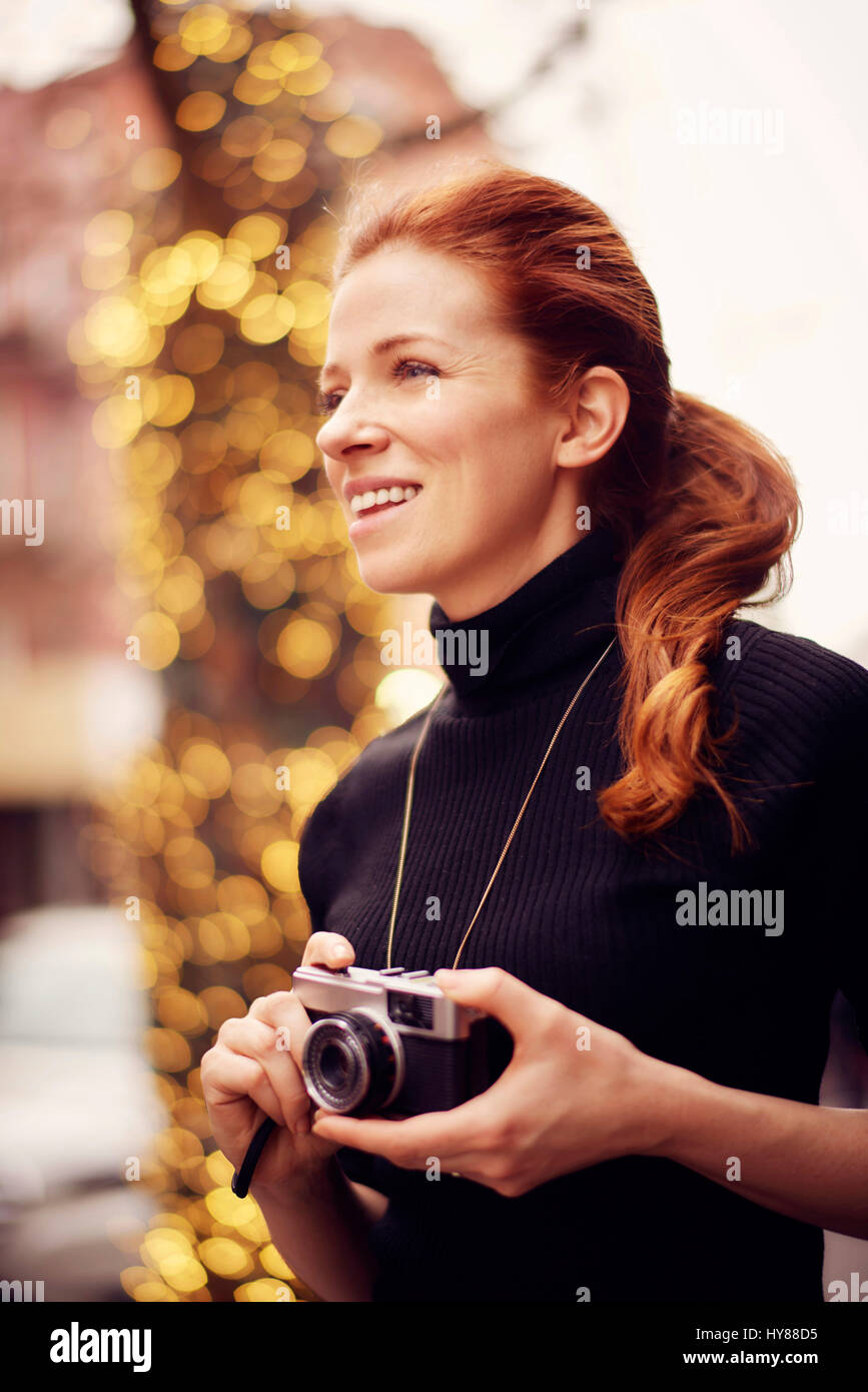 Young fashionable women with classic camera in front of lights in New York city Stock Photo
