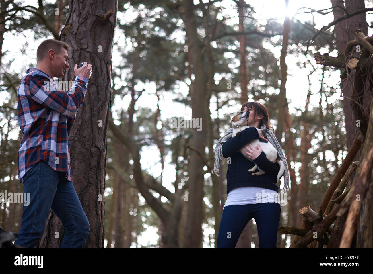 A man takes a photo of his female companion and her dog as they walk in the woods Stock Photo