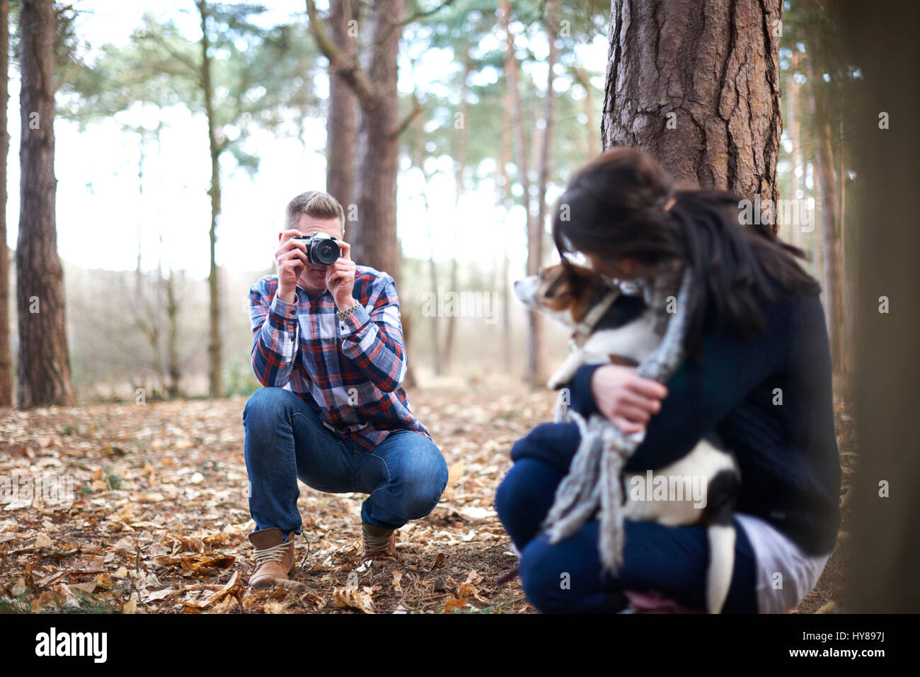 A man takes a photo of his female companion and her dog as they walk in the woods Stock Photo