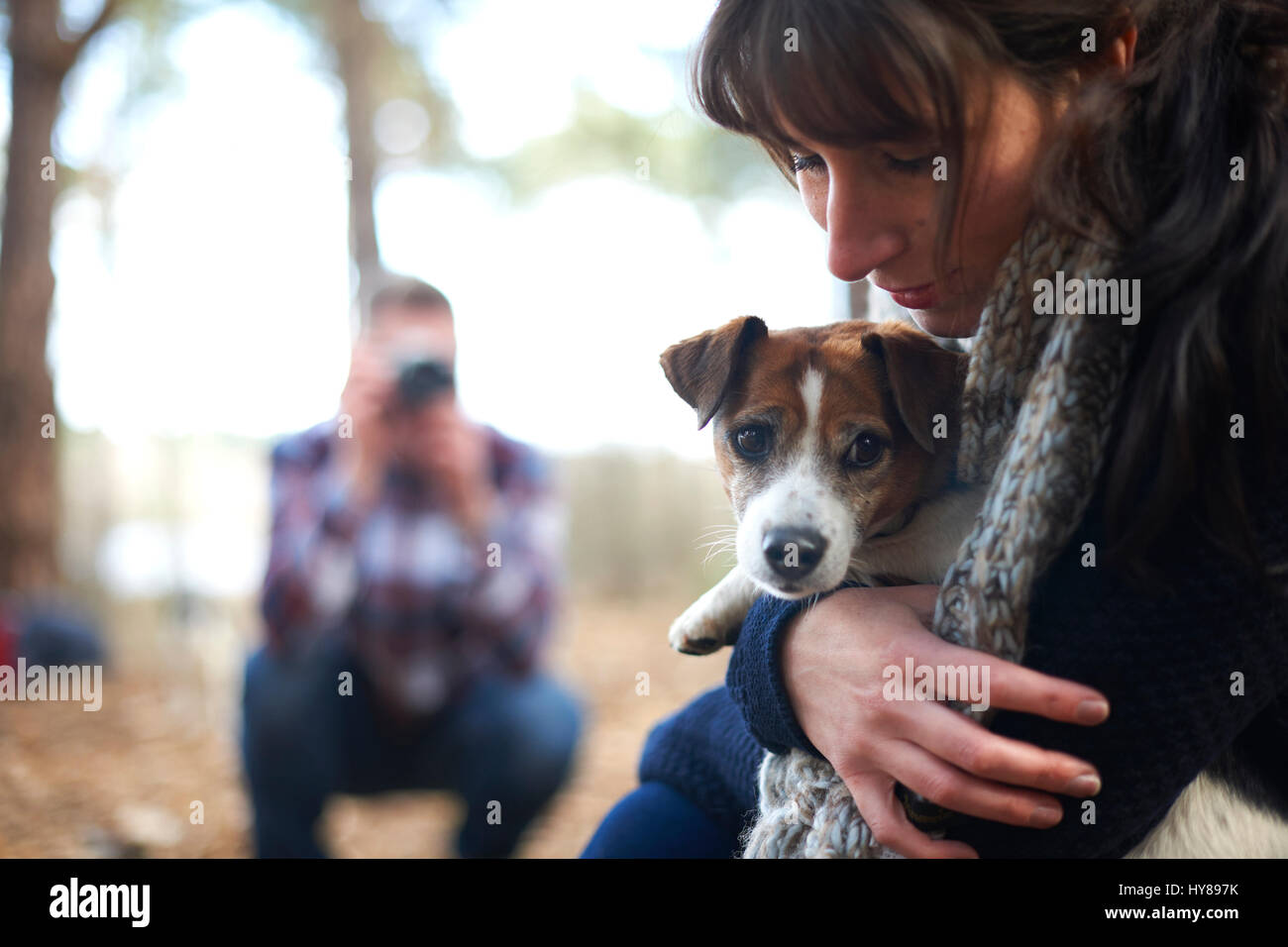 A man takes a photo of his female companion and her dog as they walk in the woods Stock Photo