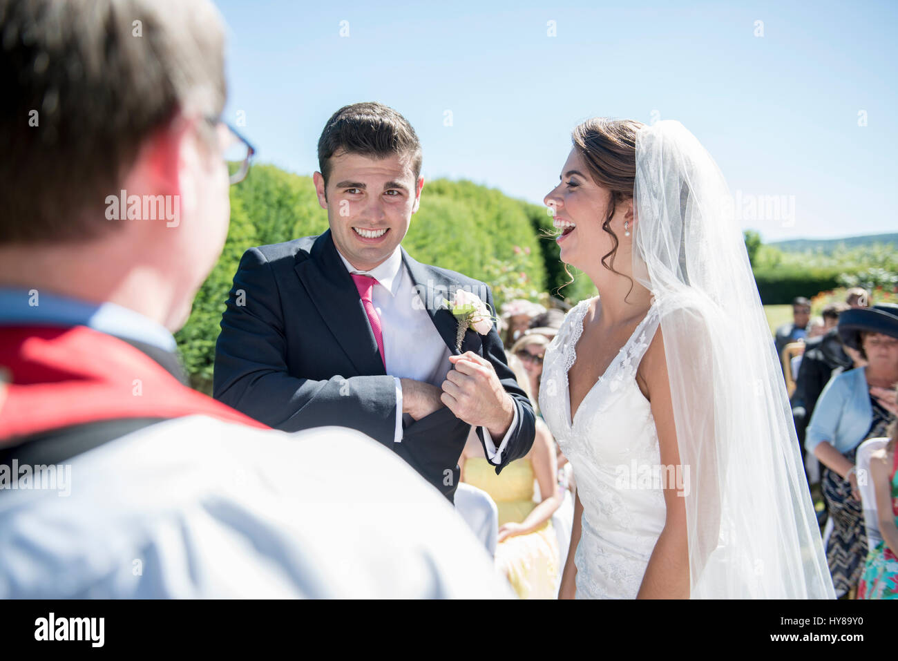 A bride and groom stand in front of a vicar at an outdoor wedding Stock Photo