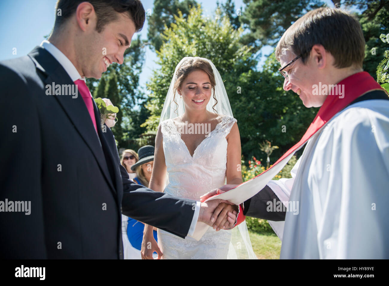 A bride and groom stand in front of a vicar at an outdoor wedding Stock Photo