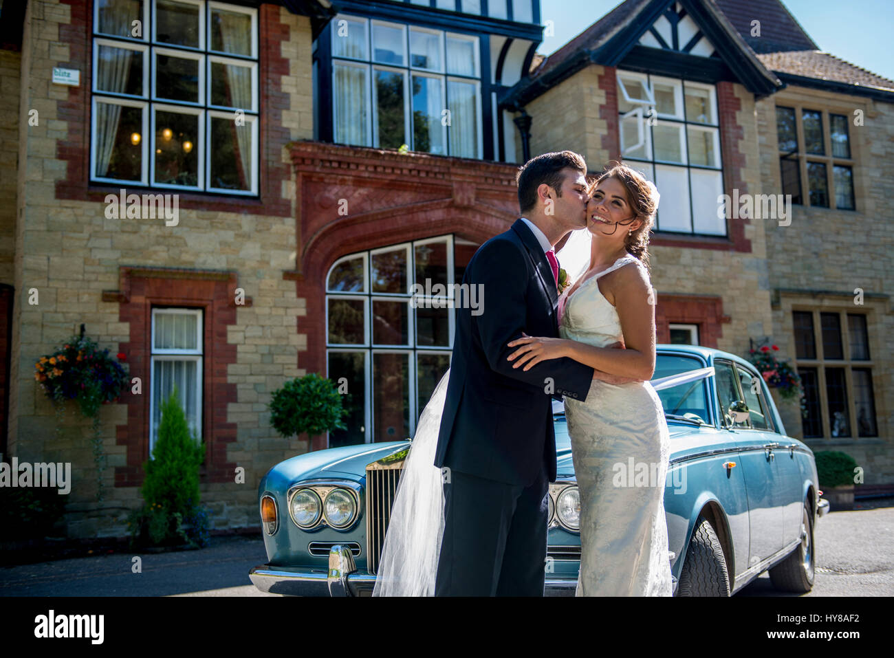 A bride and groom share a kiss on their wedding day as the wedding car awaits them Stock Photo