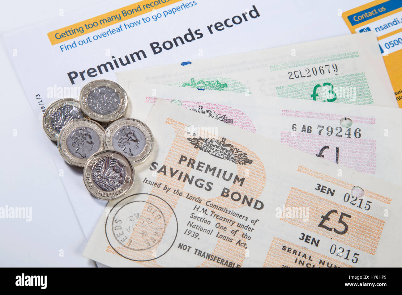 New £1 pound coins, £2 pound coins and £5 pound notes on an Premium Bond document Stock Photo