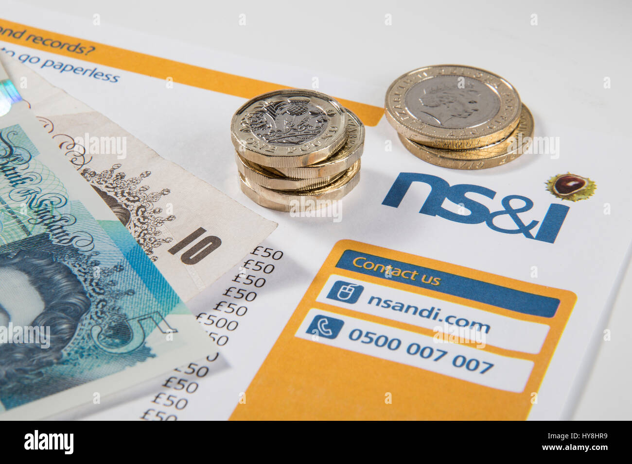 New £1 pound coins, £2 pound coins and £5 pound notes on a Premium Bond NS&I document Stock Photo