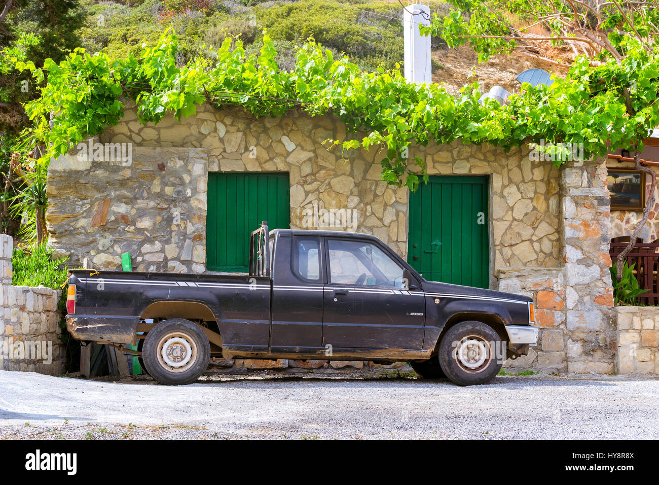 Bali, Greece - April 30, 2016: Old black pickup truck Mitsubishi L200 parked under a mountain in background of stone wall of the barn. Easy 4wd truck  Stock Photo