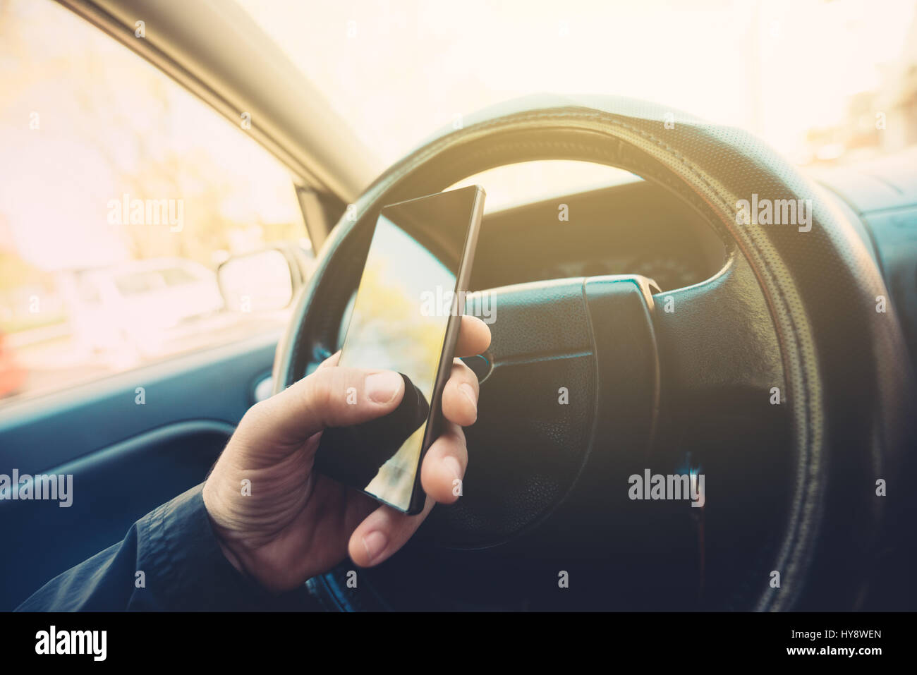Using mobile phone and driving car, smart phone in male hand on steering wheel, selective focus Stock Photo