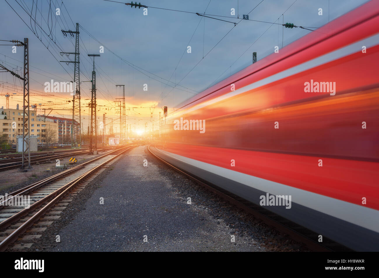 High speed red passenger train on railroad track in motion at sunset. Blurred commuter train on the railway station and sunlight. Railroad travel, rai Stock Photo