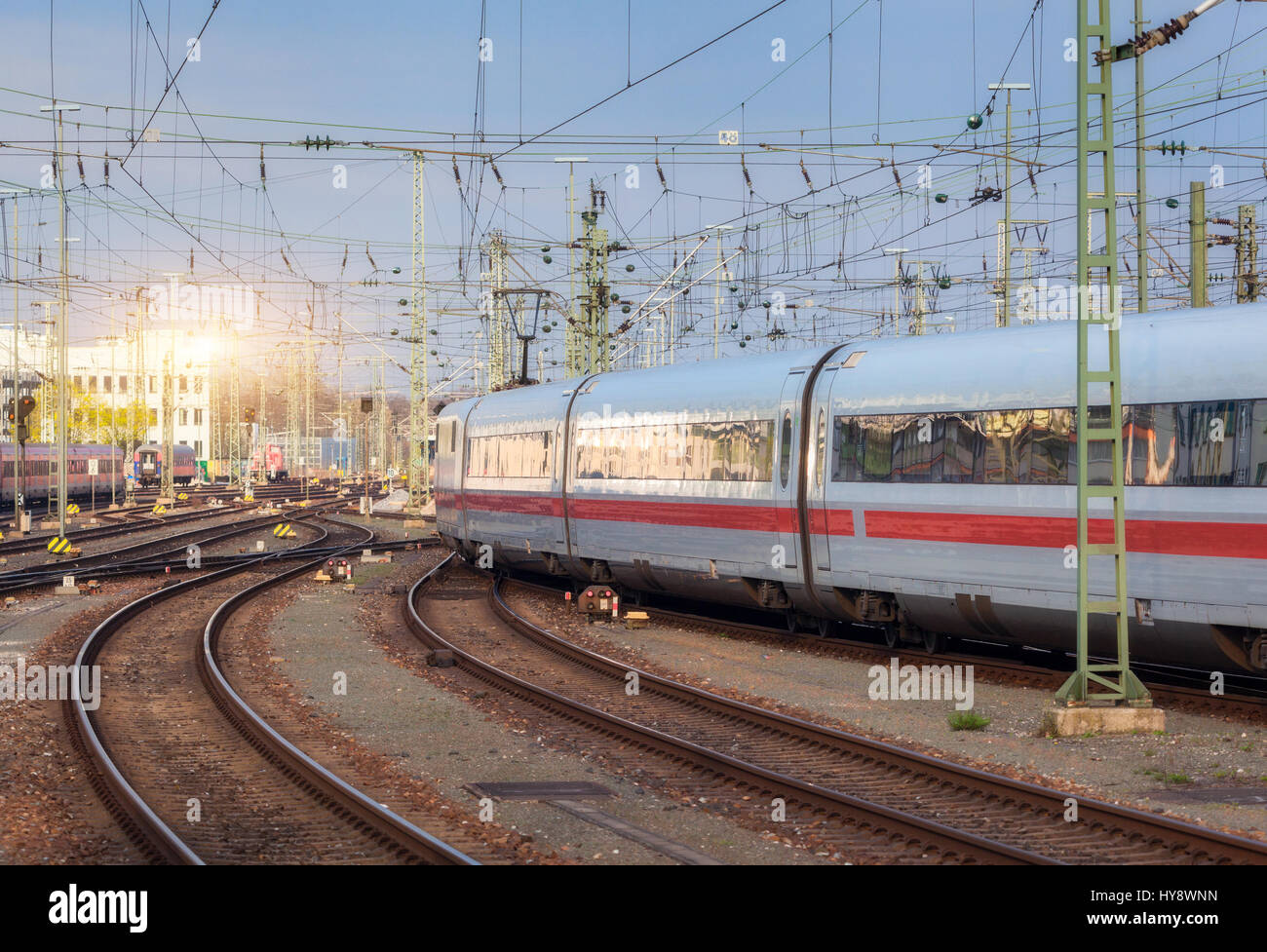 High speed white passenger train on railroad track in motion at sunset in Germany. Commuter train on the railway station in the evening. Railroad trav Stock Photo