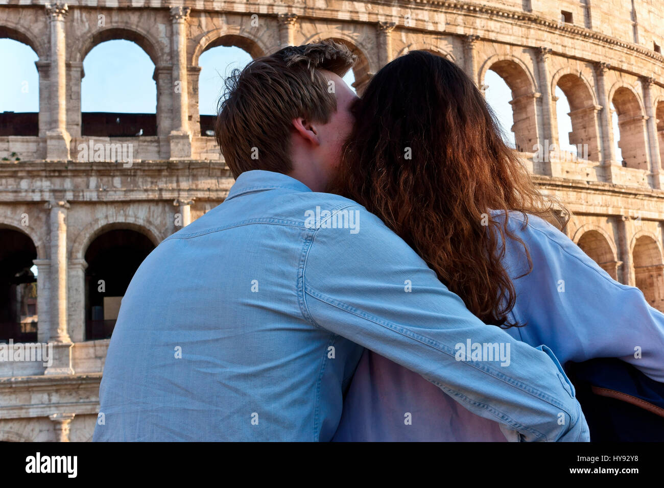 Romantic young couple embracing, arm around, looking at the Colosseum Rome. Colosseo. Rear view, seen from the back. Valentines day. Toutists. Italy Stock Photo