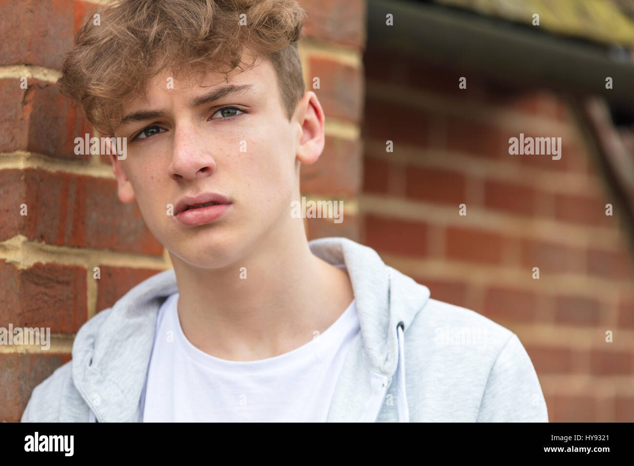Serious male boy teenager outside leaning on brick wall wearing a gray hoody Stock Photo