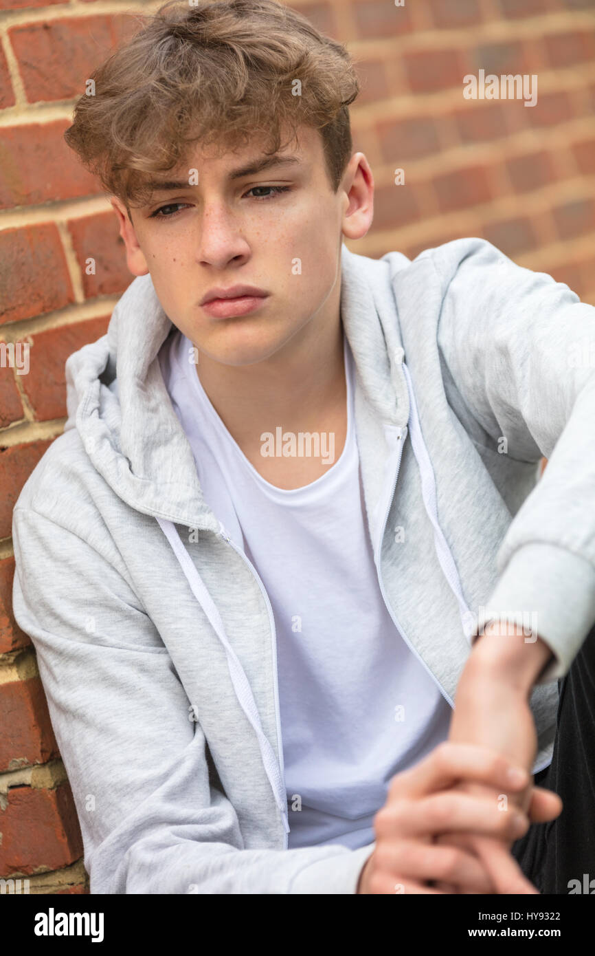 Sad depressed male boy teenager outside leaning on brick wall wearing a gray hoody Stock Photo