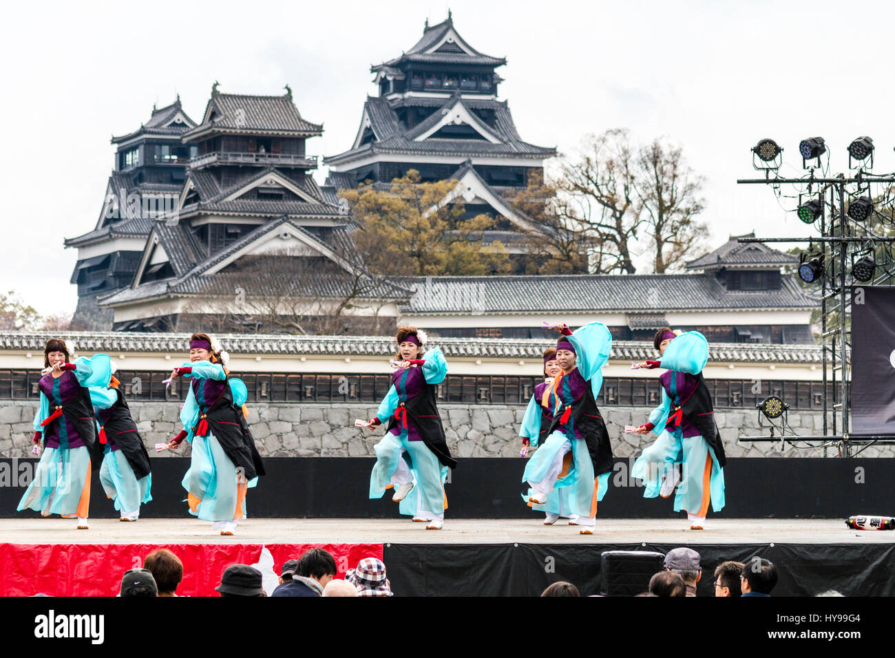 Hinokuni Yosakoi Dance Festival in Japan. team of mature women dancing on stage in black and turquoise costume with Kumamoto castle in background. Stock Photo
