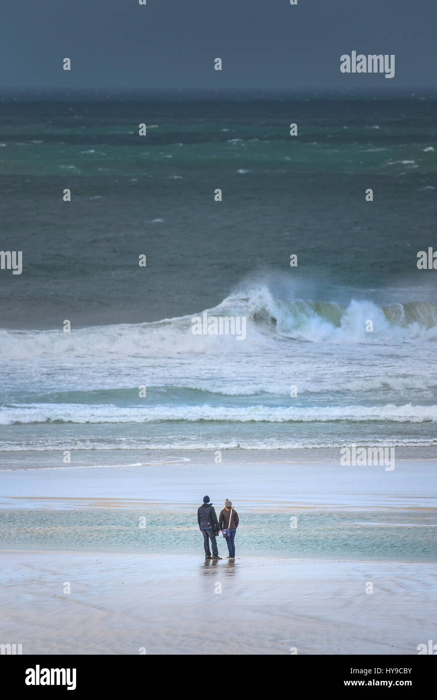 Couple Watching Looking Standing Beach Shoreline Shore Seaside Sea Waves Surf Rough seas Windy Stormy Spray UK weather Fistral Cornwall Stock Photo