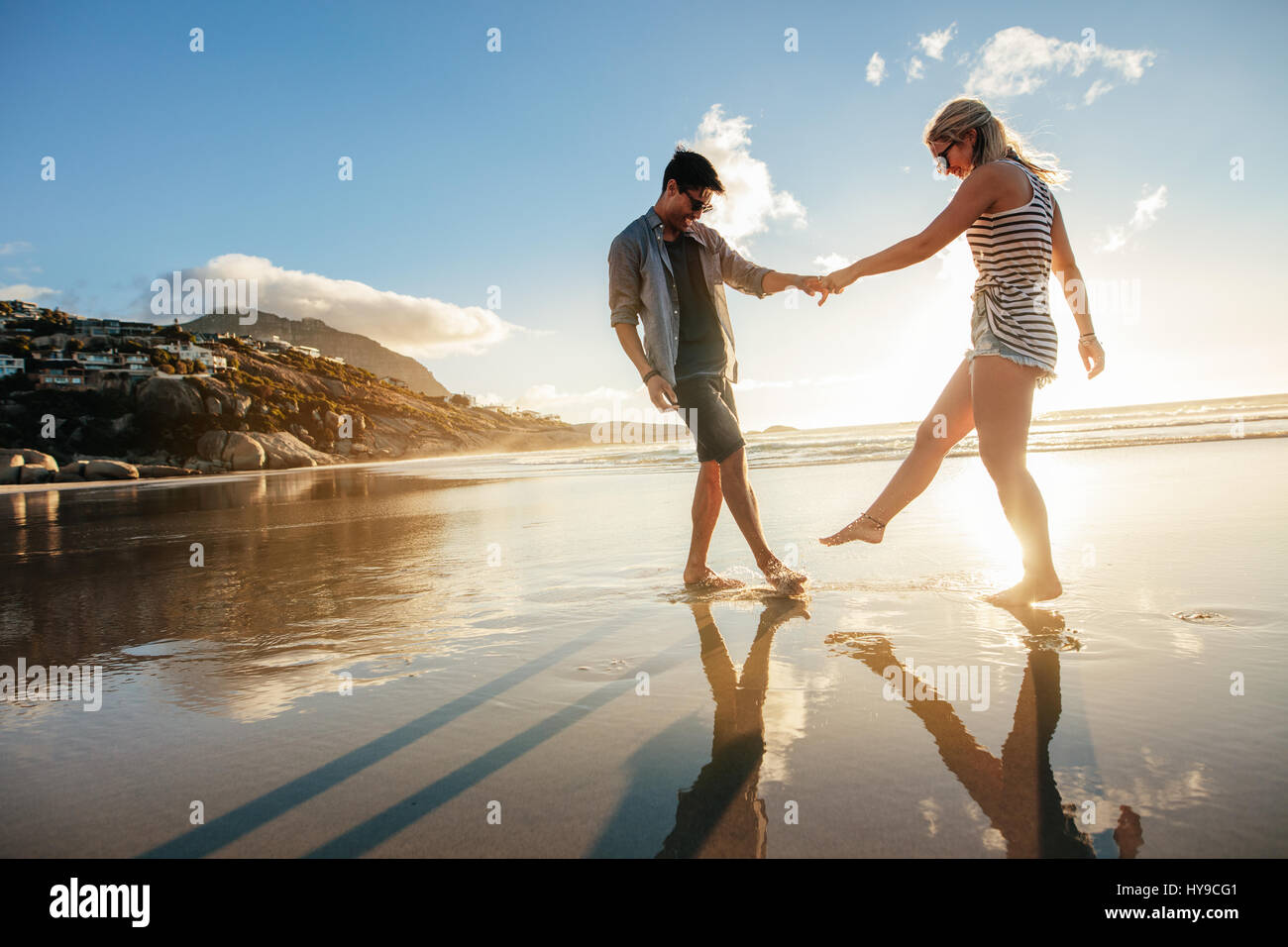 Beautiful young couple holding hands and playing on the shore. Happy young romantic couple in love having fun on beach. Stock Photo